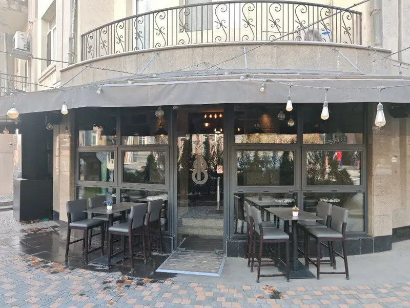 The corner terrace: high tables and grey bar chairs under the balcony